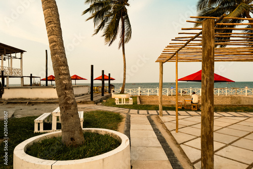 A tourist enjoying Serene Beachfront View with Palm Trees and Coastal Architecture at Bagamoyo Port, Tanzania