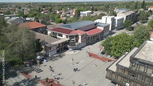 Aerial shot ascending directly over the central town square in Vrbas, Serbia. Focus on the urban plaza layout and surrounding architecture on a bright sunny day.