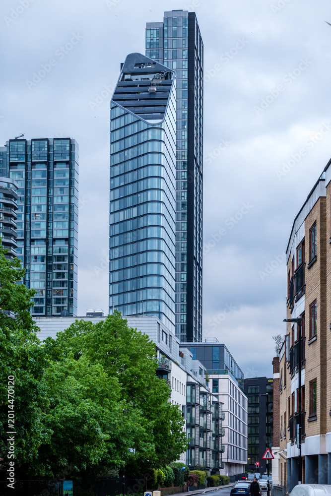Obraz premium Modern Residential Tower Rising Above Quiet Tree Lined Street in London England Urban Neighborhood Setting