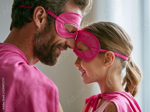Father and daughter share a fun moment wearing matching pink superhero costumes at home in the afternoon