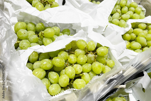 Fotografia Green grapes wrapped in white paper packaging at supermarket display
