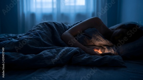 Mental health concept of a woman lying in bed at night feeling lonely and anxious while looking at her mobile phone
