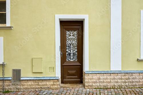 Fotografia Elegant brown door with decorative ironwork on yellow building