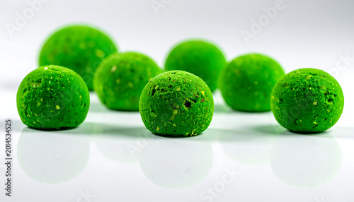 Several vibrant green spherical energy balls coated in crushed nuts and seeds, arranged on a reflective white surface with soft studio lighting