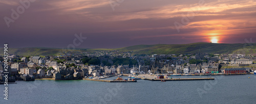 A wide panoramic view of the Lerwick waterfront and harbor at sunset with a golden sky over the coastal town of the Shetland Islands in Scotland, UK