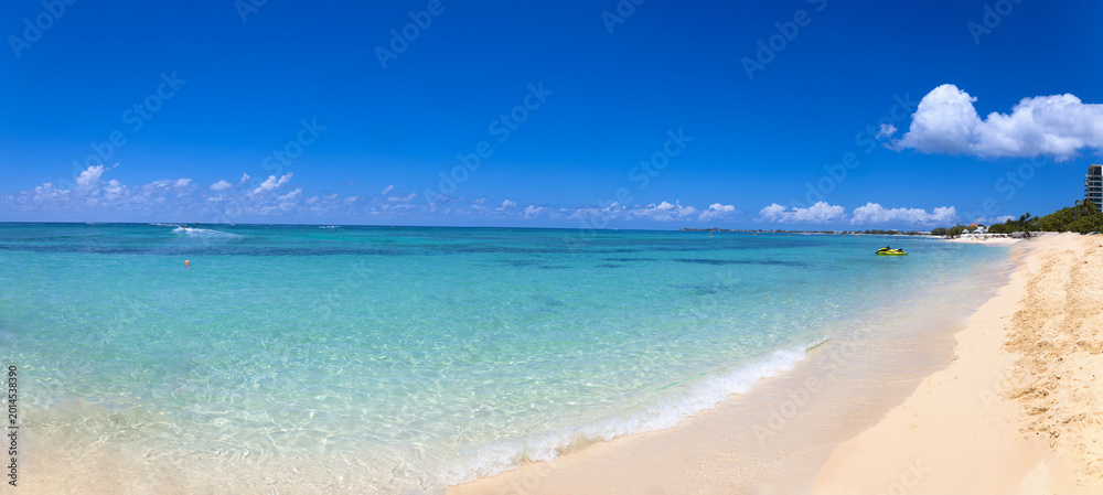 Naklejka premium Wide panoramic view of the tropical Seven Mile Beach in George Town Grand Cayman featuring crystal clear turquoise water white sand and a bright blue sky