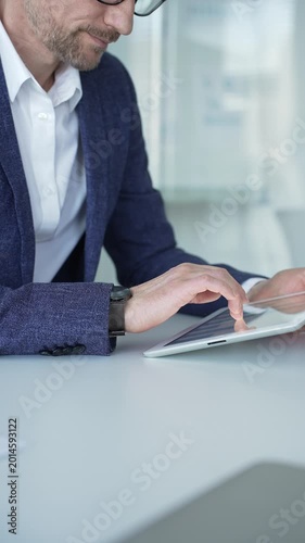 Professional businessman working on a digital tablet, interacting with graphics and data, demonstrating modern technology use and business productivity in a corporate setting