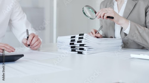 Business professionals auditing financial documents with a magnifying glass, reviewing paperwork for analysis and investigation. Audit and taxes in business