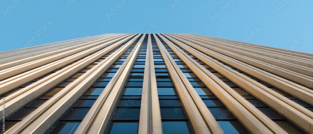 Fototapeta premium Looking up at a tall modern skyscraper's facade against a clear blue sky
