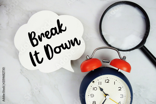 Break It Down text with magnifying glass and alarm clock on marble background