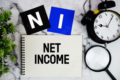 Photos NI Net Income text written on notepad with alarm clock and magnifying glass on m