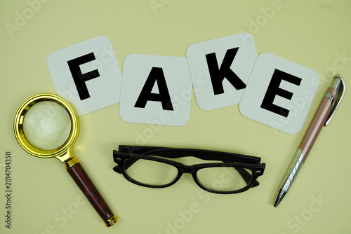 Fotografija FAKE alphabet letters with magnifying glass, eye glasses and pen on yellow backg