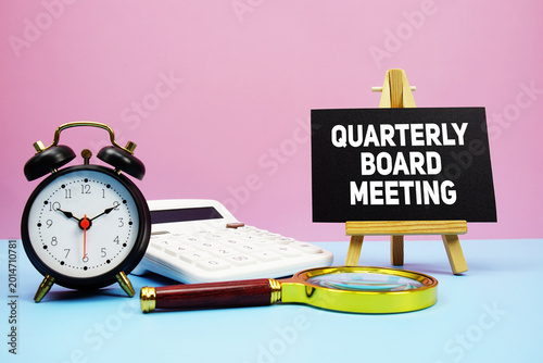 Photos Quarterly Board Meeting text with calculator, alarm clock and magnifying glass o