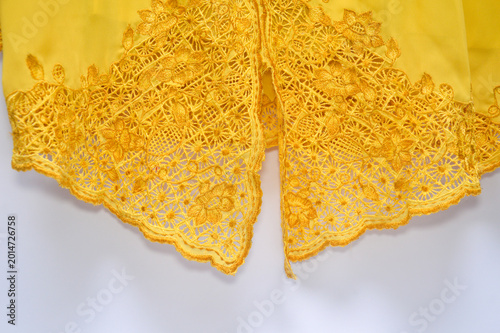 Close up of yellow fabric with intricate floral lace embroidery. Detailed textile background featuring traditional needlework and elegant golden yellow thread.