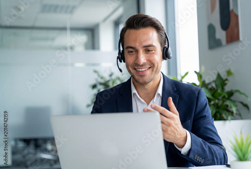Smiling call center agent with a headset working on a laptop in a modern office