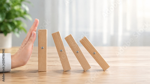 Hand stops falling wooden blocks representing financial concepts in debt management and risk prevention with calm and responsible approach in bright office environment