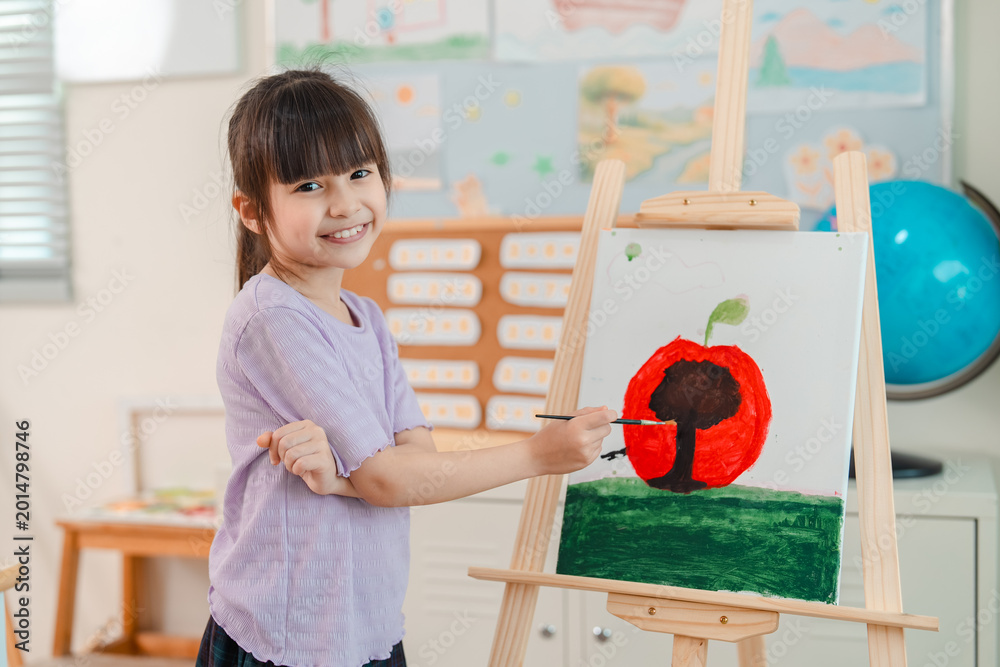 Naklejka premium Back to school and education concept of smiling girl painting apple on easel in classroom art lesson