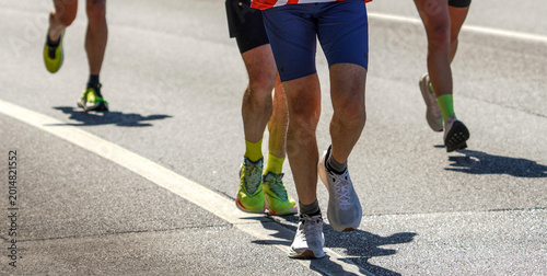 Canvas Print Road race runners approaching in bright sunlight with strong shadows on asphalt