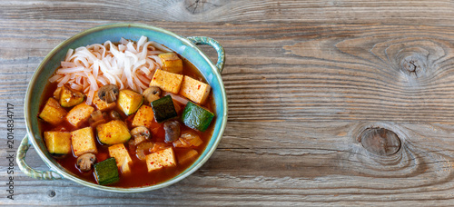 Vegan version of kimchi soup with tofu and rice noodles. Rustic wooden background - a banner with space for additional content. 