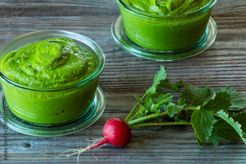 Two glass jars with radish greens pesto, fresh whole radish next to them - rustic wooden background.