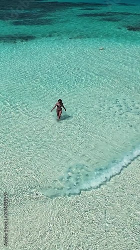 Woman walking through clear shallow turquoise ocean water on Maldives beach under sunny sky. Concept of travel, vacation, summer, tourism, relaxation, tropical lifestyle. Vertical video