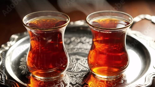 Two glasses of dark amber tea served in traditional tulip-shaped clear glasses on an ornate silver tray, warm inviting atmosphere, rich beverage