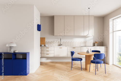 Canvastavla Bright minimalist kitchen interior with beige cabinets, blue accents, wooden dining set and large window in modern apartment