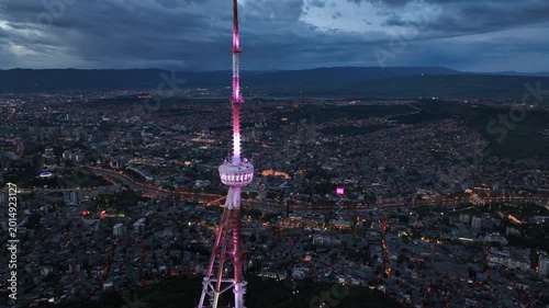 Aerial view of the Funicular Restaurant at Mtatsminda Park during sunset. Dynamic drone shot of a TV tower with Tbilisi city in the background.