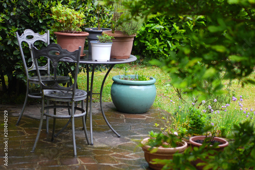 Pots and plants in garden on old fashioned iron table and chair, sunlight, Bergamo, Italy.