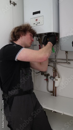 Vertical screen apartment technician repairing heating boiler and checking water system connections during routine maintenance inside modern home utility room