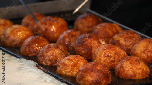 Canvas Print Rows of golden brown Takoyaki octopus balls being flipped and cooked in a specia