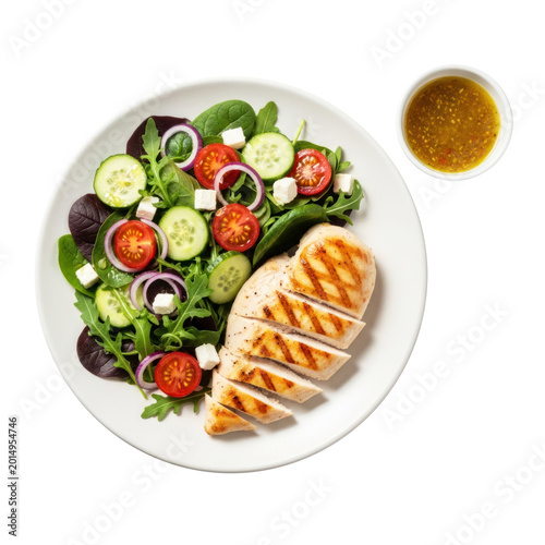 A white plate holds a grilled chicken breast and a mixed green salad. The salad contains sliced cucumbers, cherry tomatoes, red onion rings, feta cheese, and baby greens.