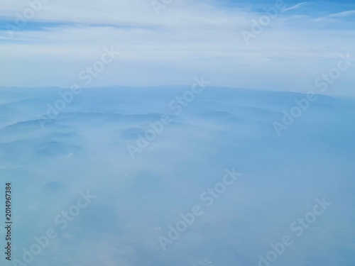 Aerial landscape with layered mountain ranges fading into blue atmospheric haze. Minimal and serene natural background with soft gradients, ideal for travel, nature, climate, and abstract concepts.
