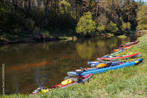 Group of colorful inflatable kayaks parked on the grassy bank of a river in the forest