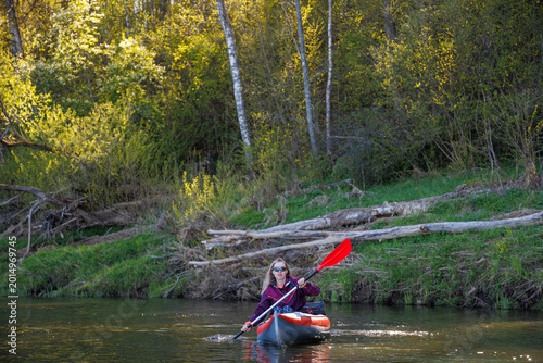 Woman in a kayak navigating through the water against a background of spring forest and logs