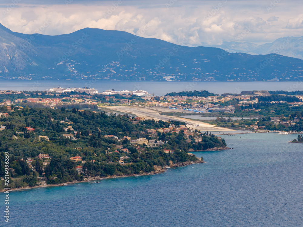 Fototapeta premium Panoramic High Angle View of Corfu International Airport Runway and Port with Large Cruise Ships in the Distance - Scenic Mediterranean Island Landscape with Mountains and Ionian Sea in Greece