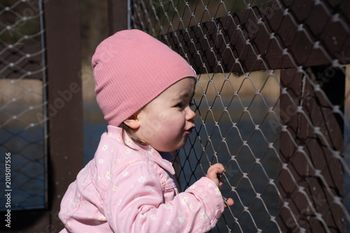 Foto young toddler in a pink beanie and daisy-patterned jacket peers and grips a chai