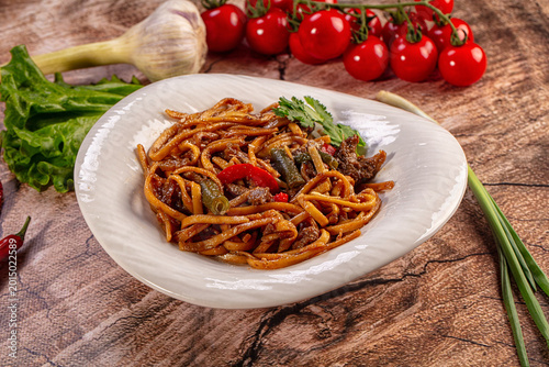 Fotografija Savory stir fried noodles with beef and vegetables on a rustic wooden table