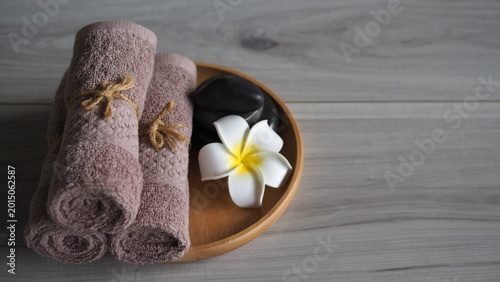 Photography Brown rolled towels tied with jute rope on wooden plate, zen stones, and frangipani flower on gray wood background