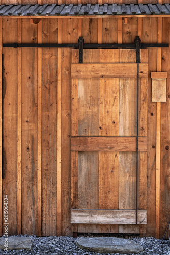 Contemporary Japanese building using traditional staining to preserve natural golden color of wood-plank facade with matching rustic sliding door, name plate, slatted roof, and gravel stones.