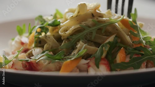 Slow motion eat pesto fettuccine with crab meat on plate closeup
