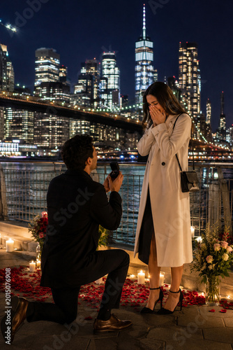 Man Proposing to Woman in Front of Illuminated City Skyline at Night
