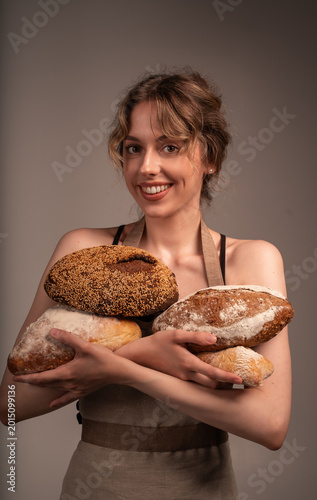 Baker woman holding fresh artisan sourdough bread loaves, proudly presenting handmade rustic whole grain bakery products