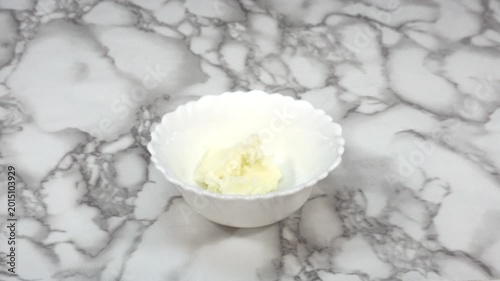 Hand Holding Bowl of Butter on Marble Countertop Close Up for Cooking and Baking Ingredients, Close-up of a hand holding a white bowl containing butter on a marble kitchen countertop.
