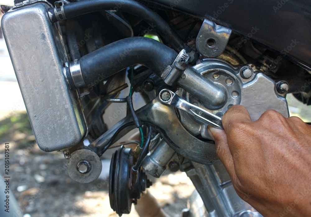 Fototapeta premium Close-up of a mechanic's hand using a wrench to repair a motorcycle engine. Maintenance and DIY repair of a liquid-cooled motorbike. Automotive mechanical workshop concept