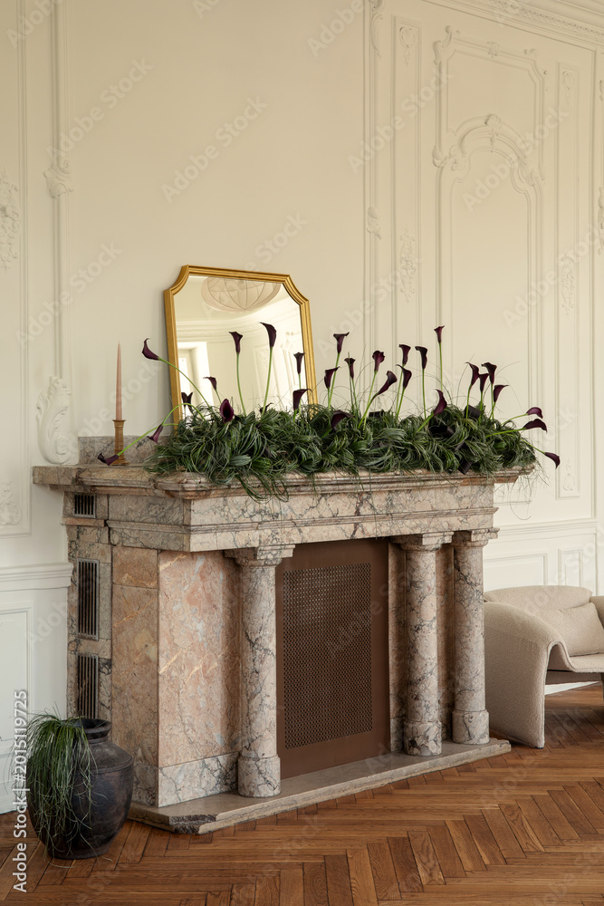Fototapeta premium Elegant Room Interior with Fireplace Decorated with Dark Calla Lilies, Greenery and Gold Mirror