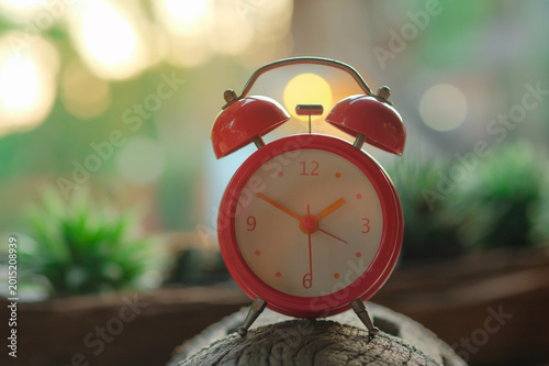 Retro Alarm Clock on Wooden Surface: A charming retro red alarm clock sits perched on a rustic wooden surface, with a blurred natural background creating a sense of calm and nostalgia.