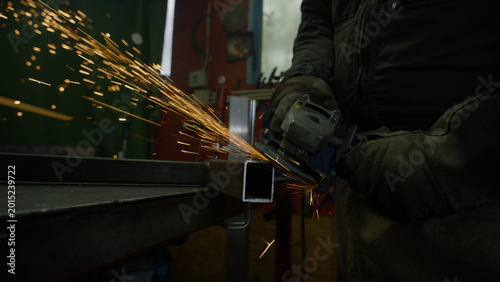 Bild auf Leinwand Welder processing a metal pipe with a grinder, making sparks