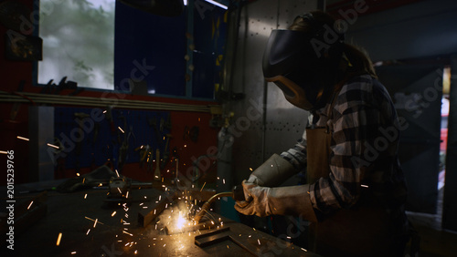 Skillful and dedicated female welder welding steel in a dark home workshop. Small business startup concept.