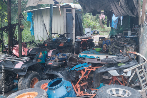 Abandoned shed with broken machinery and scattered tools. Worn tires lie beside broken equipment and debris. Blue bucket sits among scattered metal fragments